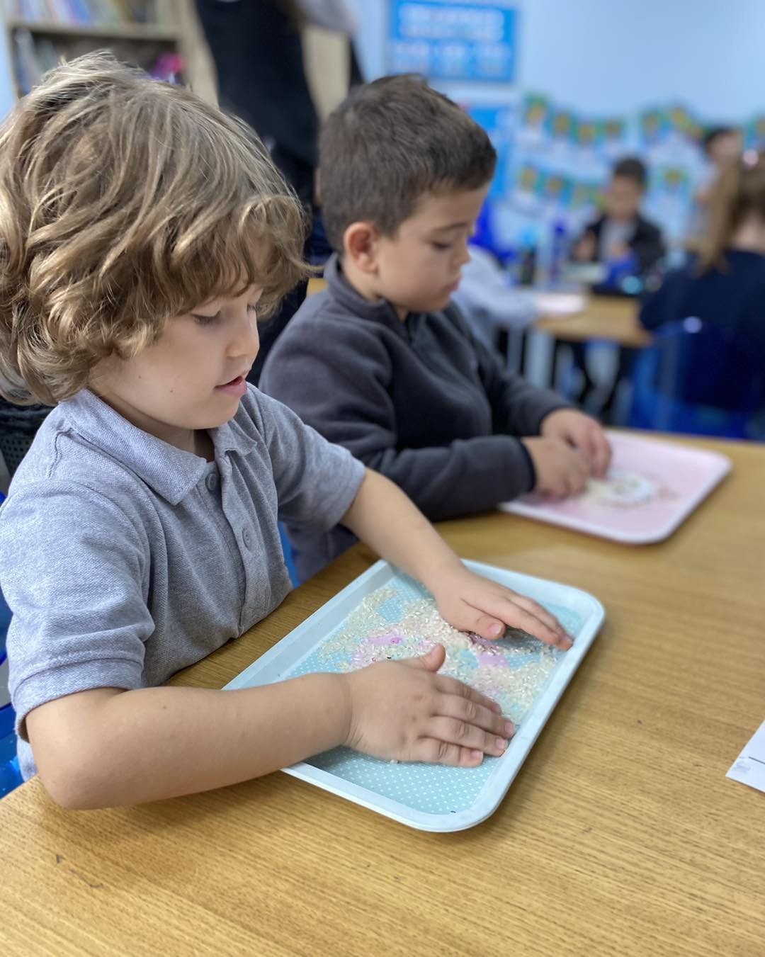 The kindergarten students practice writing their letters with a sensory rice tray